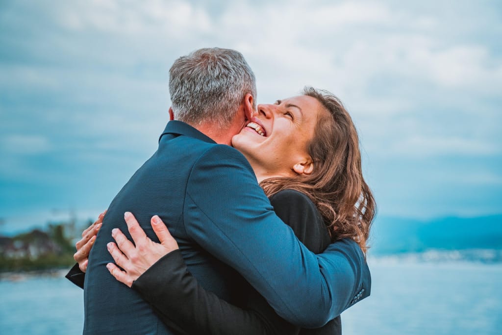 Mann und Frau umarmen sich, ein See ist im Hintergrund