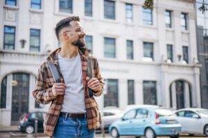 Junger Mann in einem Flanellhemd läuft durch die Stadt und lächelt dabei.
