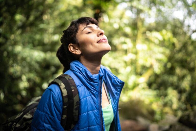 Eine Frau schlißet ihre Augen im Wald und genießt den Moment