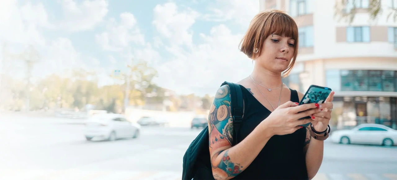 Fau mit kurzen roten Haaren und Tatoos läuft mit Handy durch die Stadt