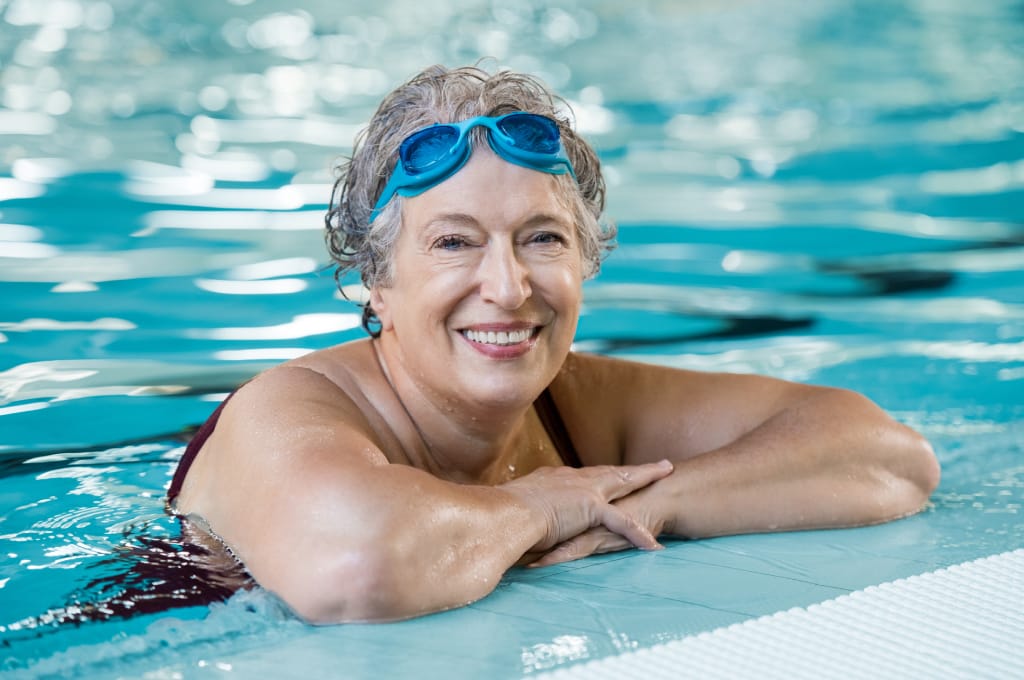 Älterer Frau mit Parkinson im Schwimmbecken mit Schwimmbrille