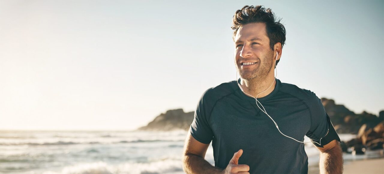 Mann mit Kopfhöreren joggt am Strand entlang