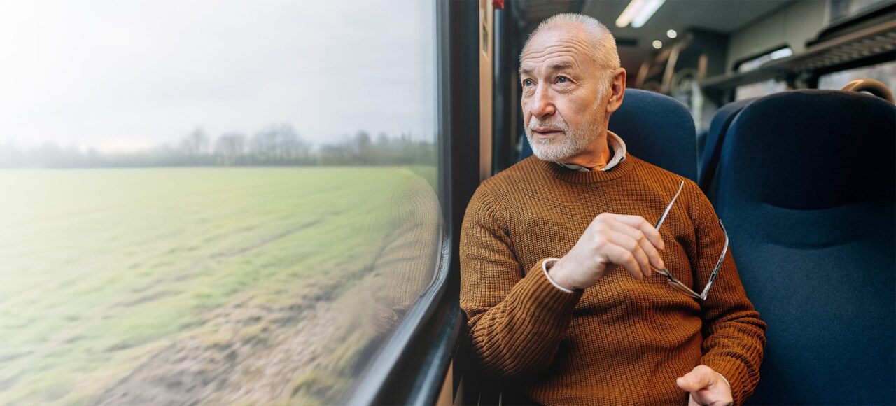 Älterer Mann sitzt im Zug und schaut aus dem Fenster