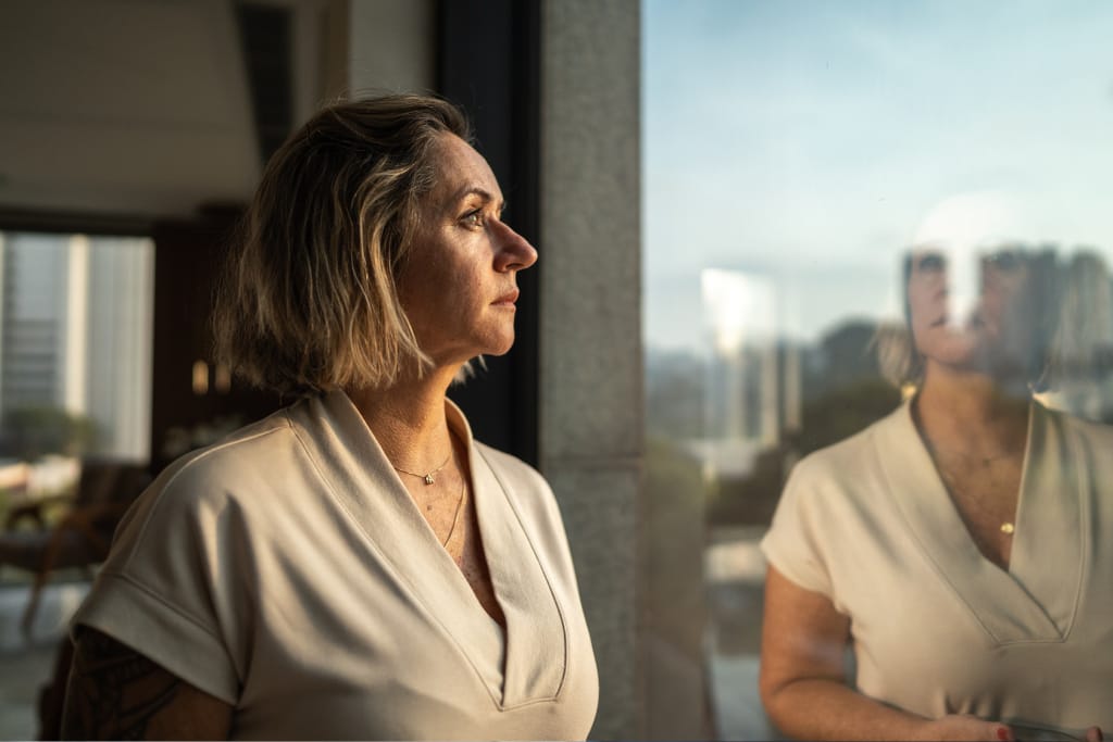 Frau mit blonden schulterlangen Haaren schaut aus dem Fenster