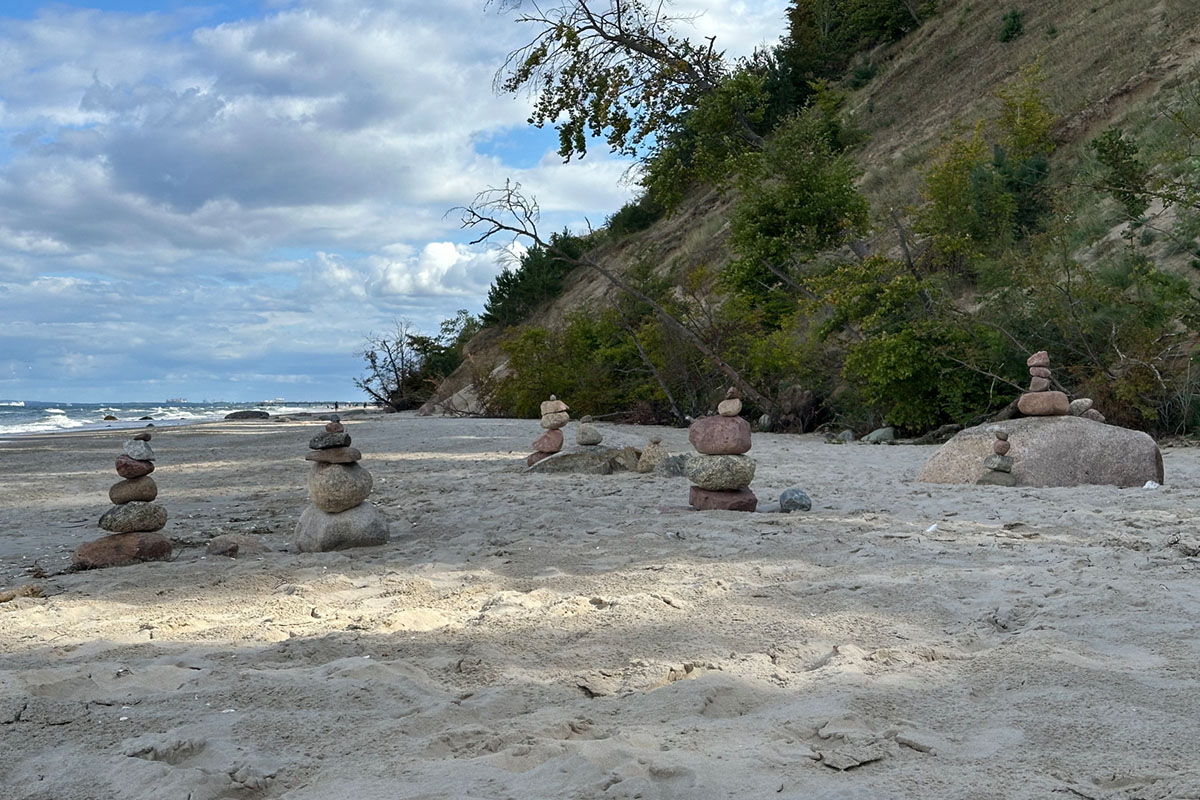 Steinmännchen stehen auf einem Sandstrand vor einer bewaldeten Steilküste