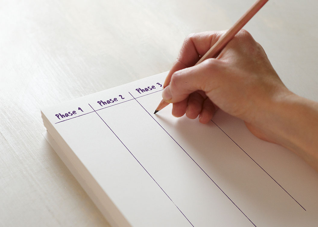 Eine Hand mit einem Bleistift macht Notizen auf einem Block