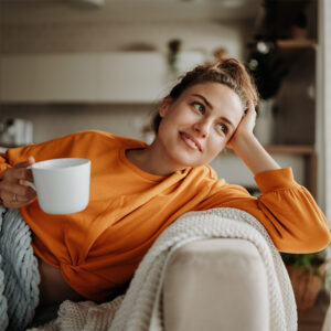 Frau liegt gemütlich auf dem Sofa mit einer Tasse Tee.