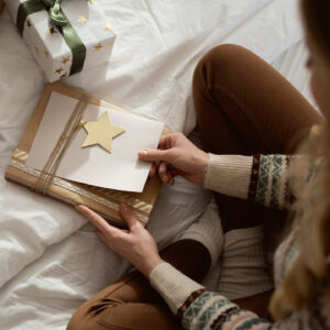 Junge Frau sitzt auf dem Bett mit Weihnachtspäckchen