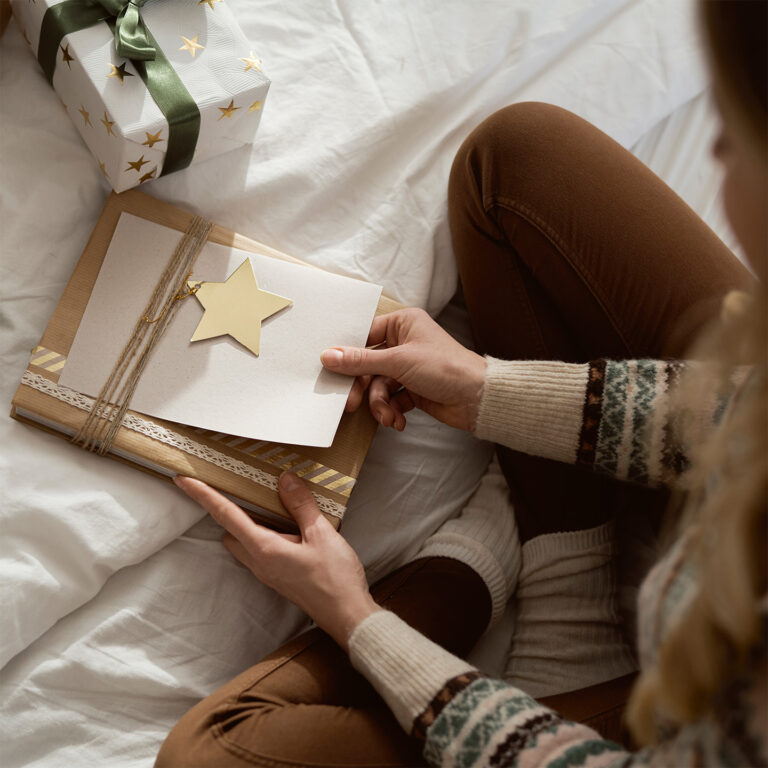 Junge Frau sitzt auf dem Bett mit Weihnachtspäckchen