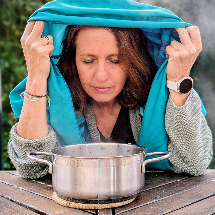 Frau inhaliert vor einem Kochtopf mit einem Handtuch über dem Kopf