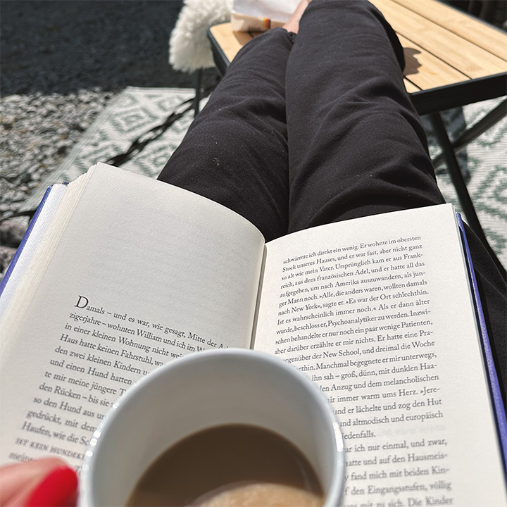 Blick auf ein augeschlagenes Buch und eine Kaffeetasse auf dem Schoß einer Frau