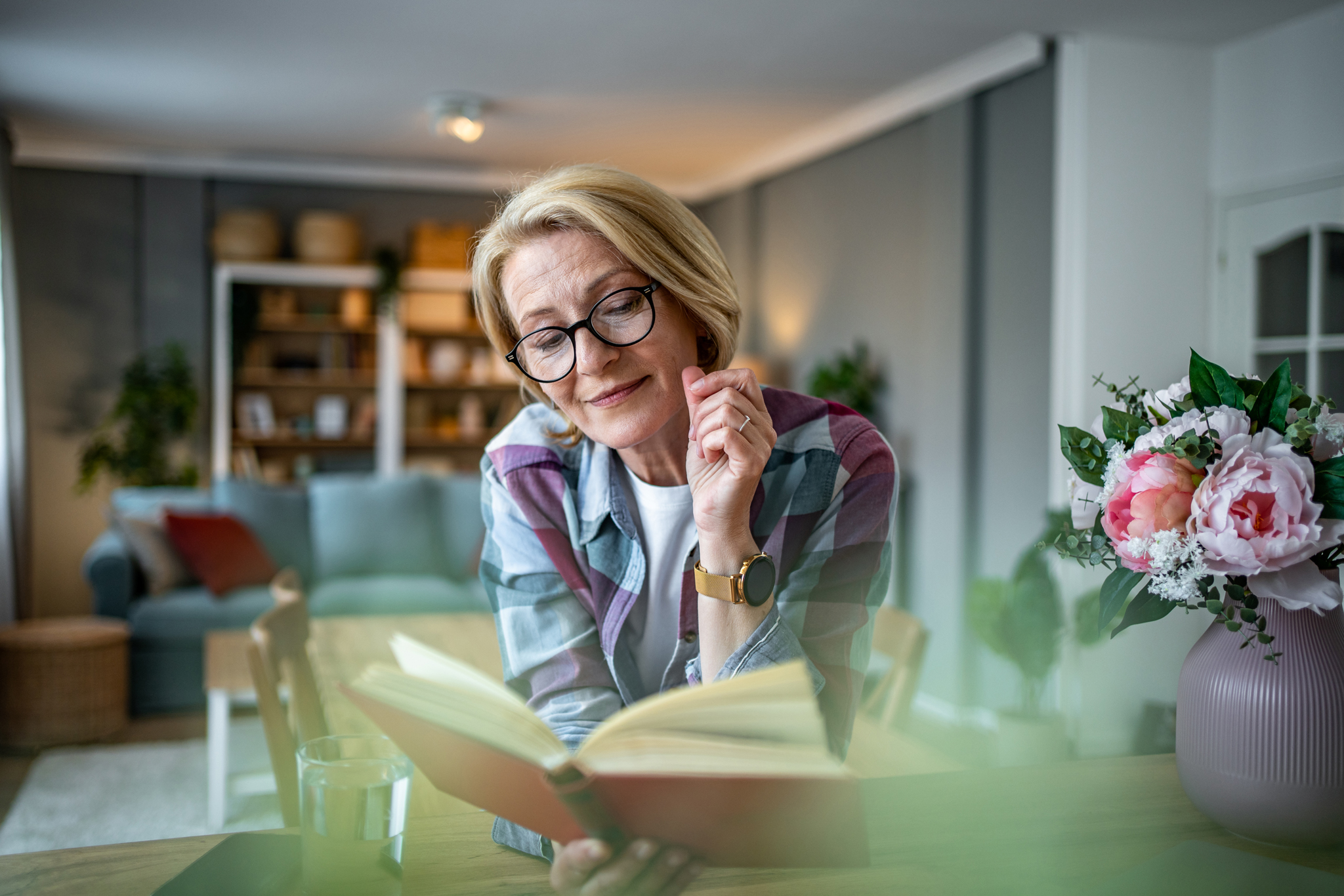Eine Frau mit blonden kurzen Haaren und gr&uuml;nem Star tr&auml;gt eine Brille und liest ein Buch