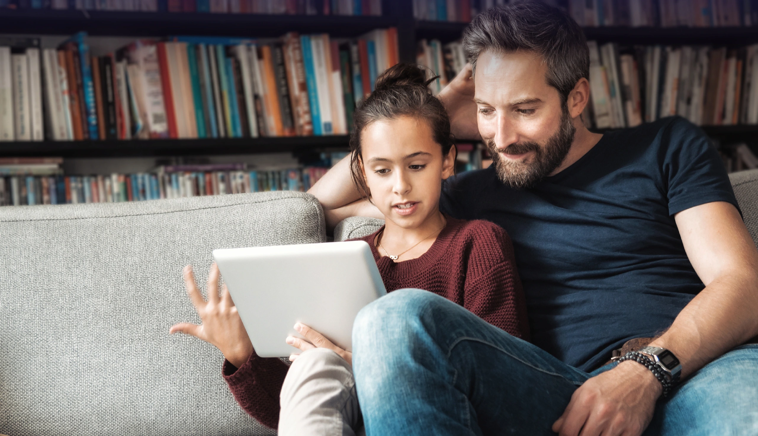 Ein Vater sitzt mit seiner Tochter auf dem Sofa und sie informieren sich am Tablet über die Diagnose Rheuma