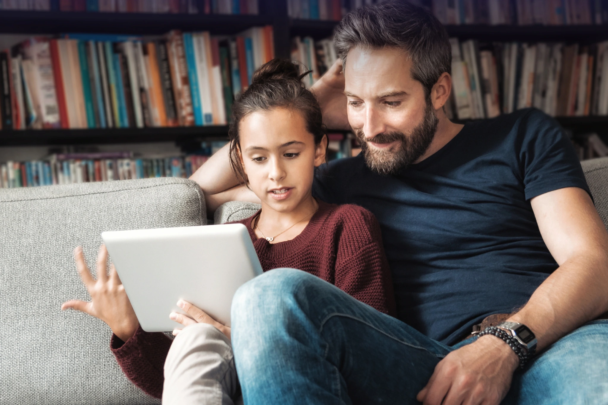 Ein Vater sitzt mit seiner Tochter auf dem Sofa und sie informieren sich am Tablet über die Diagnose Rheuma