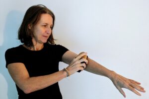 Frau in schwarzem T-Shirt streicht mit einer Massagebürste über ihren ausgestreckten Unterarm.