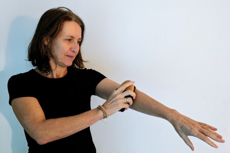 Frau in schwarzem T-Shirt streicht mit einer Massagebürste über ihren ausgestreckten Unterarm.