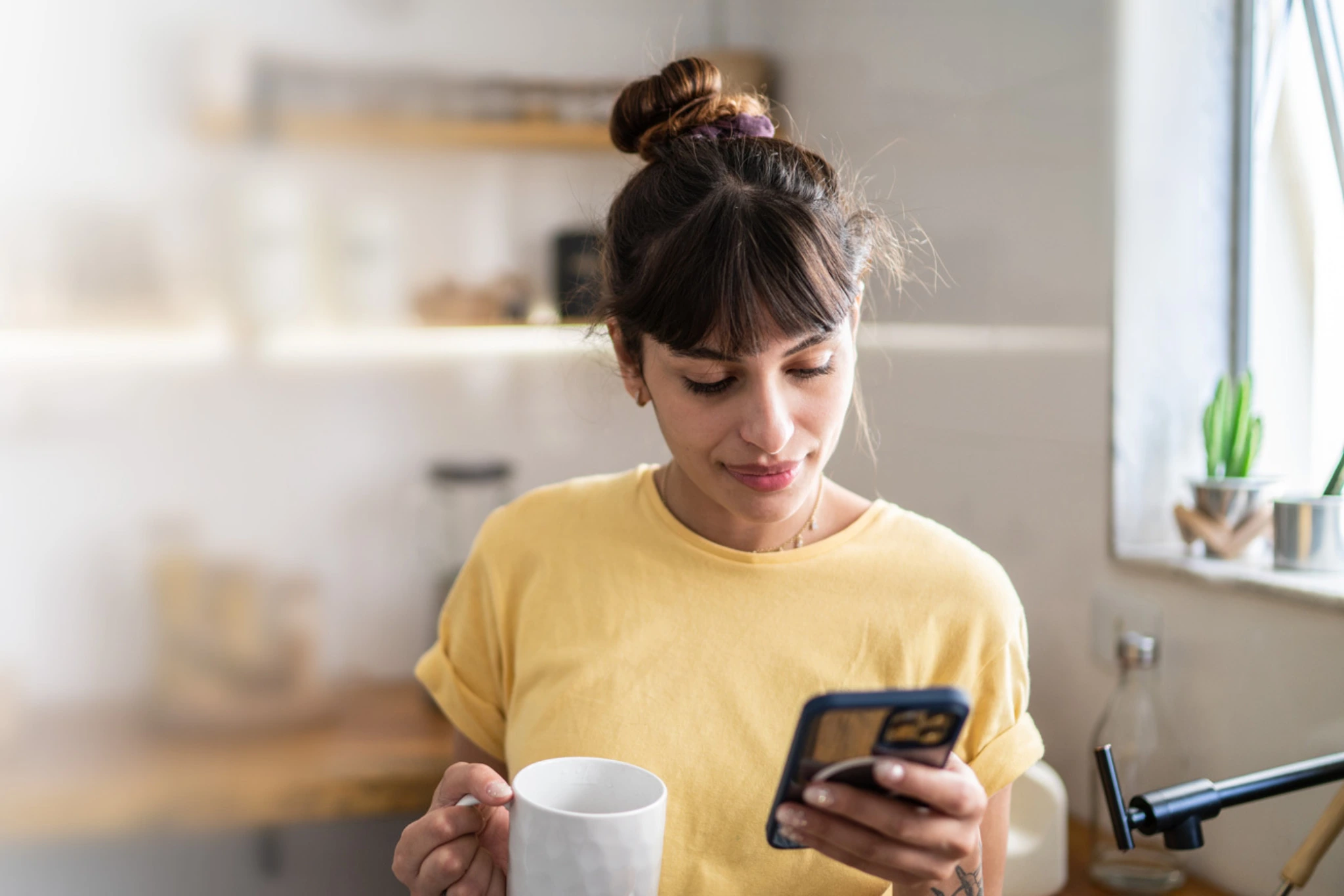 Eine Frau mit gelbem Tshirt trinkt einen Kaffee und schreibt eine Nachrict am Handy