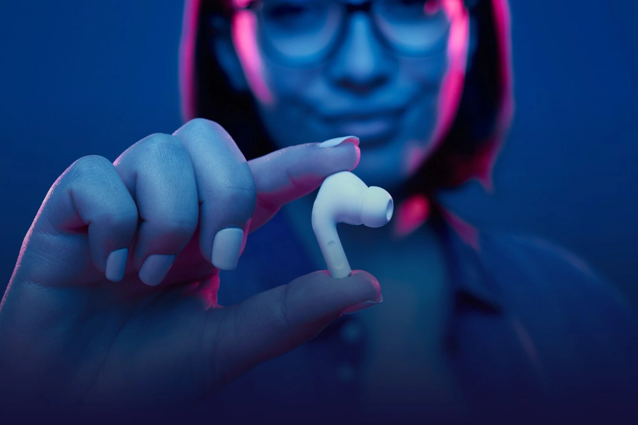 Eine Frau mit roten kurzen Haaren hält einen AirPod zwischen den Fingern.