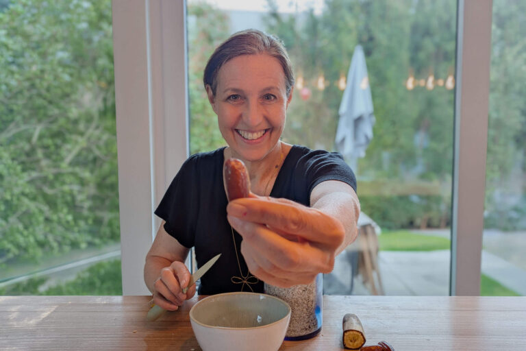 Tanja Multinu hält eine Dattel in die Kamera und sitzt vor einer Schüssel am Esstisch