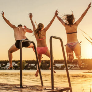 Familie springt bei schönem Wetter die Hände in die Luft reißend in einen Pool.