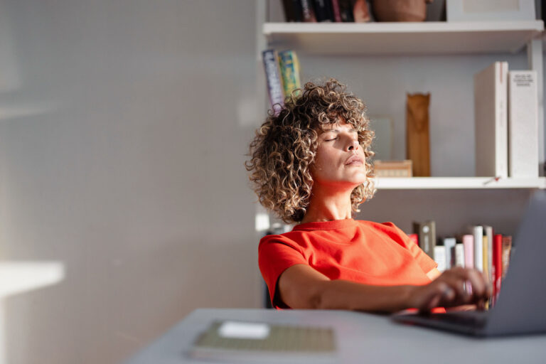 Frau entspannt sich am Homeoffice-Schreibtisch im Sonnenlicht