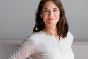  Frau Anfang 50 in weißem Pullover steht vor einer weißen Wand