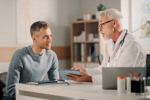 Mann Mitte 40 mit grauem Oberteil unterhält sich mit seinem Arzt zu Therapieoptionen bei Parkinson