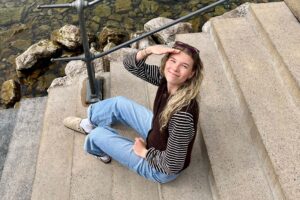 Migränepatientin Leonie sitzt draußen auf einer Steintreppe und blickt in die Kamera.